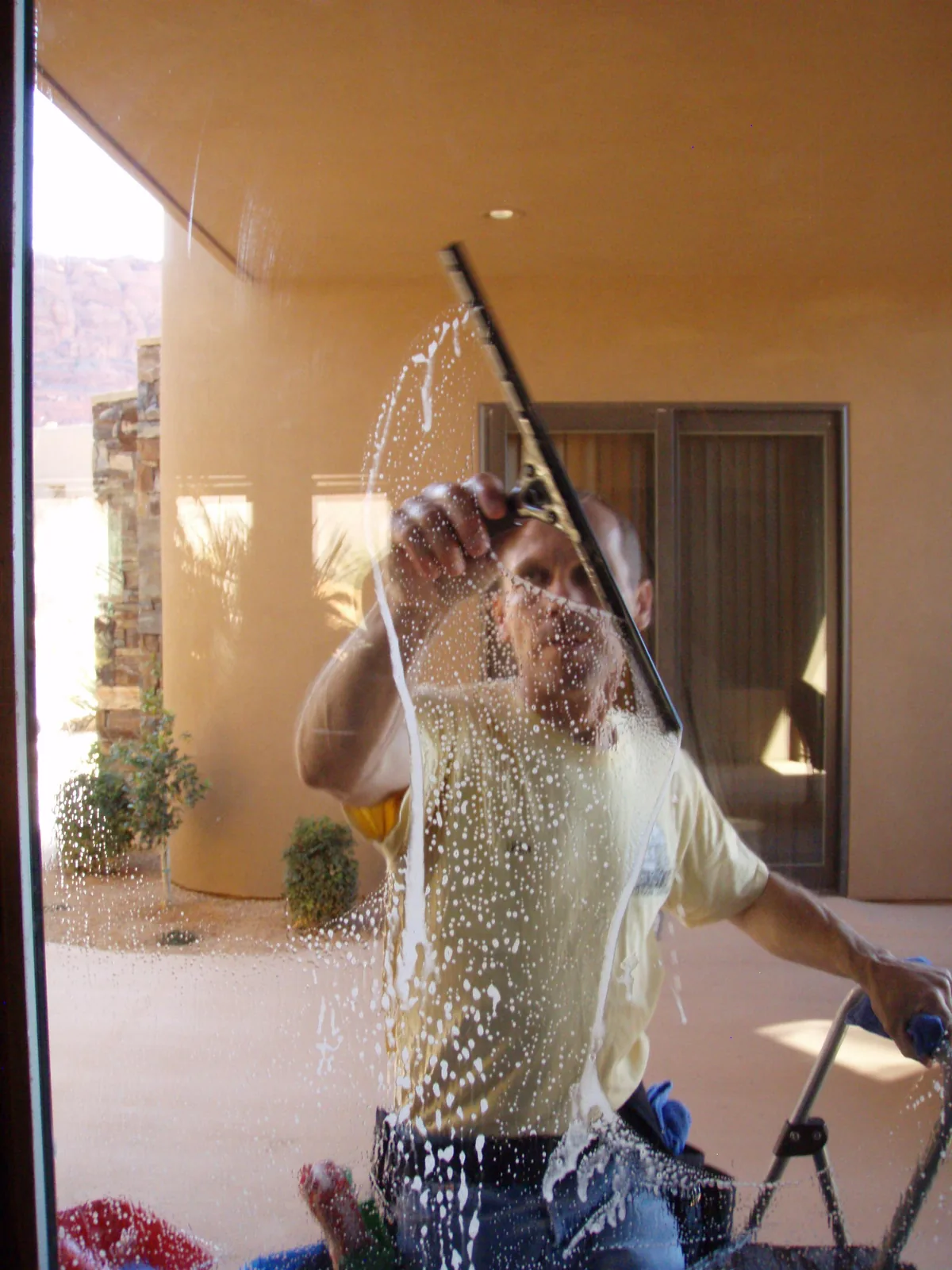 Jim squeegeeing soapy water off a glass patio door at a stucco home