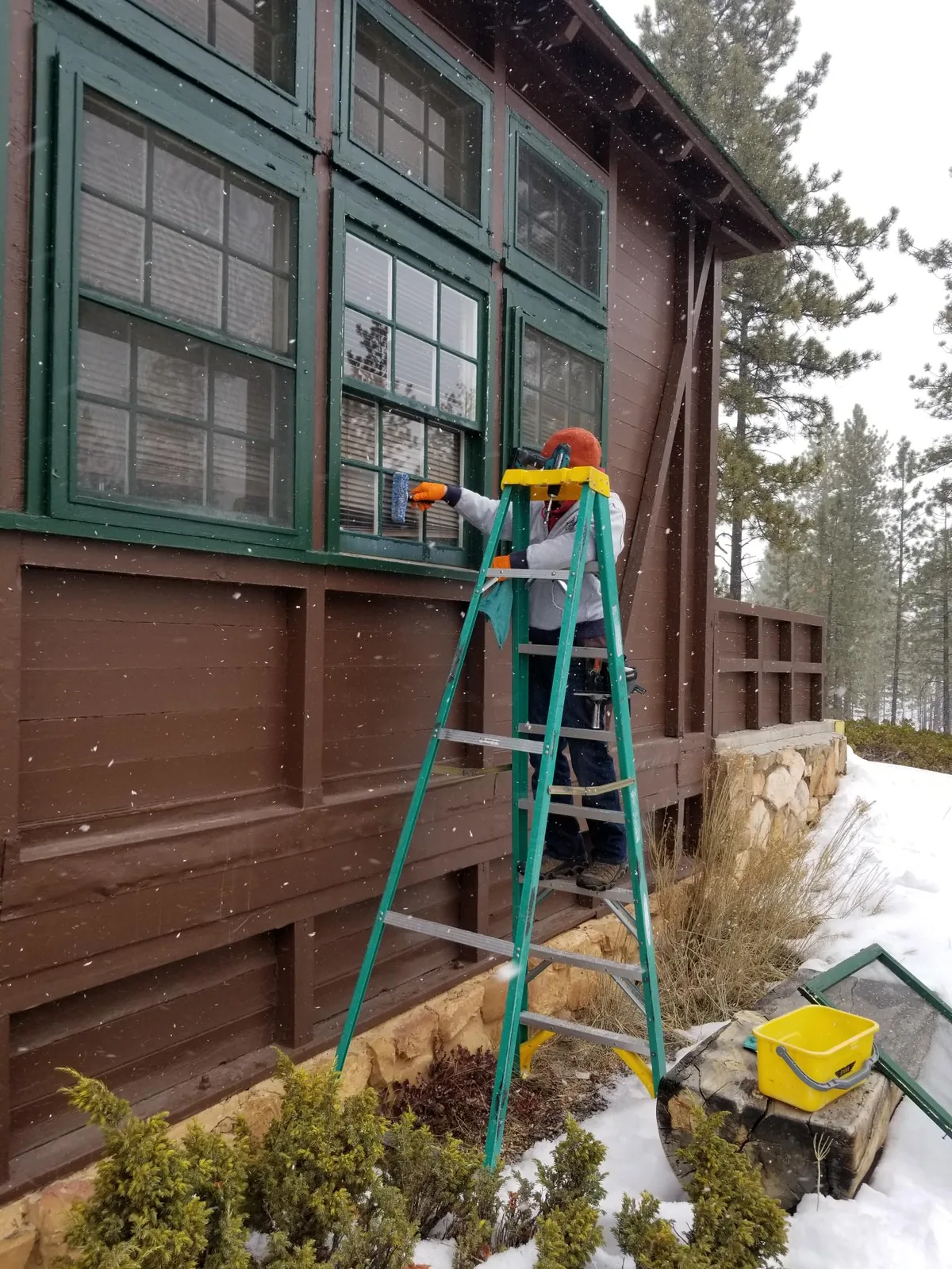 Lodge windows cleaned from a step ladder in falling snow.