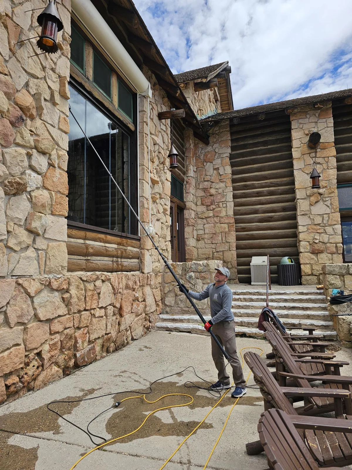 Window cleaner using a water-fed pole on tall windows of a stone and log lodge